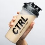 Uma mão segurando uma shakeira de whey sabor baunilha