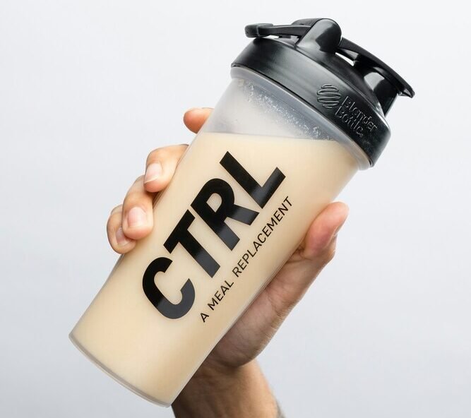 Uma mão segurando uma shakeira de whey sabor baunilha
