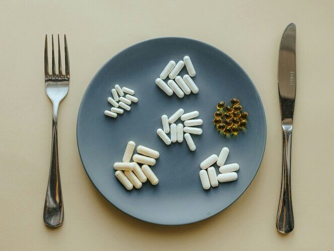 Um prato com várias cápsulas de suplementos para emagrecer com garfo e faca ao lado